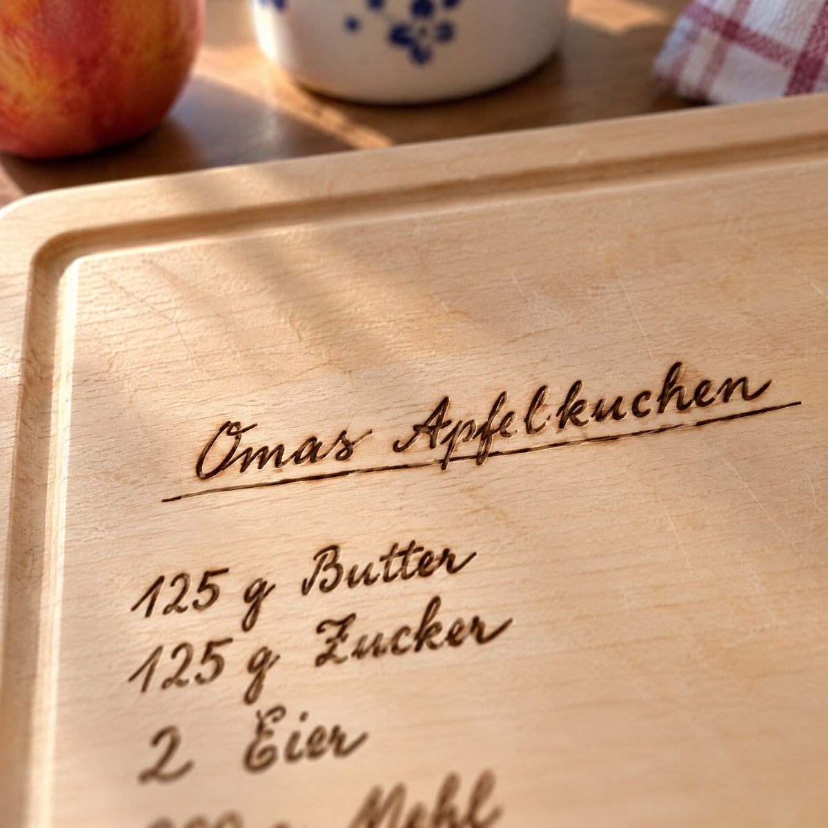 Nahaufnahme der Gravur: Titel Omas Apfelkuchen in Handschrift auf hellem Holz